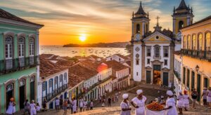Vista panorâmica do nascer do sol em Paraty, Rio de Janeiro, com igrejas históricas, ruas de pedra, turistas e mar ao fundo, durante manhã ensolarada.